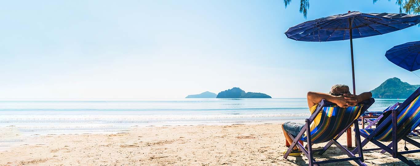 ontspannen jonge man in een strandstoel kijkt voor zich uit over de zee naar een eilandje